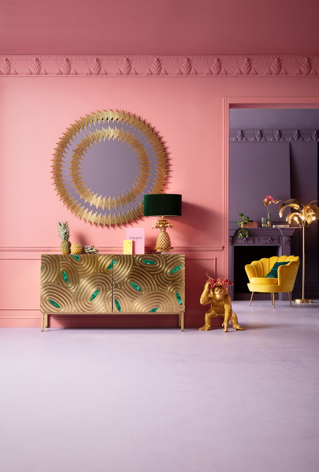 Goldene Deko-Figur eines Affen als Butler, der eine Schale mit Früchten trägt, in einem stilvoll eingerichteten Raum mit rosa Wänden und goldenen Akzenten. Perspektive: Frontalansicht.