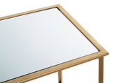 Nahaufnahme eines rechteckigen Beistelltischs mit Spiegelglasplatte und goldfarbenem Metallrahmen, leicht von oben in schräger Perspektive fotografiert