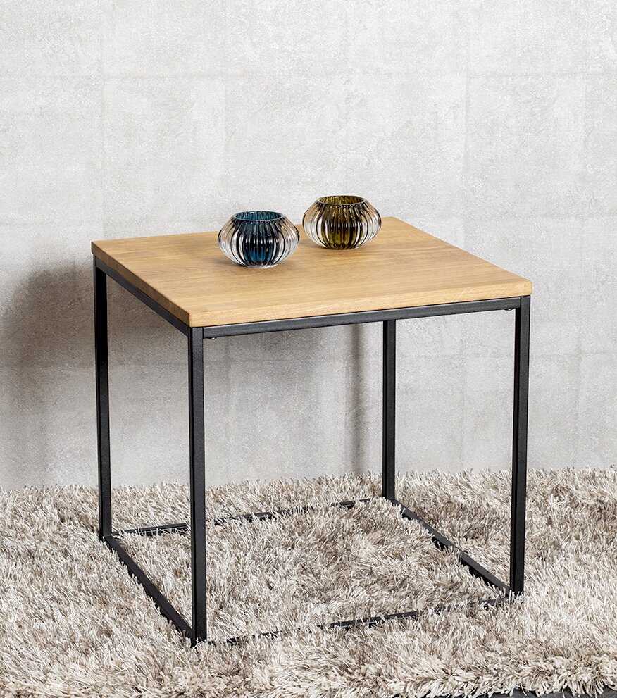 Moderner quadratischer Beistelltisch mit heller Holzplatte und schwarzem Metallgestell auf flauschigem Teppich, mit zwei kleinen geriffelten Glasvasen obenauf; Perspektive: leicht schräg von vorne in Augenhöhe