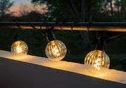 Lichterkette mit klaren, kugelförmigen LED-Lampen, die an einem Geländer bei Dämmerung aufgehängt sind.