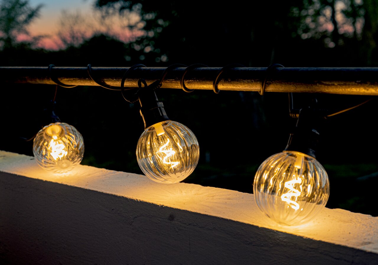Lichterkette mit klaren, kugelförmigen LED-Lampen, die an einem Geländer bei Dämmerung aufgehängt sind.