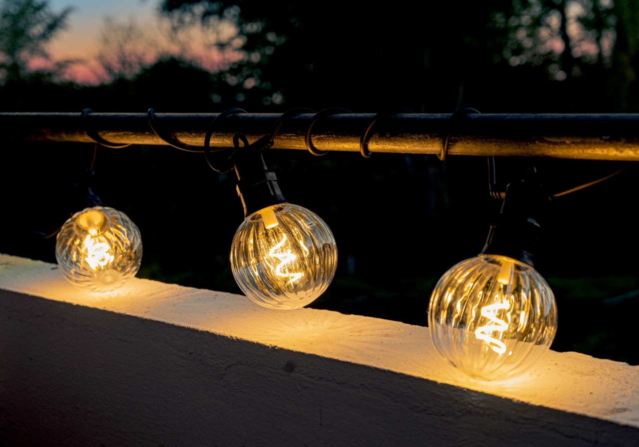 Lichterkette mit klaren, kugelförmigen LED-Lampen, die an einem Geländer bei Dämmerung aufgehängt sind.