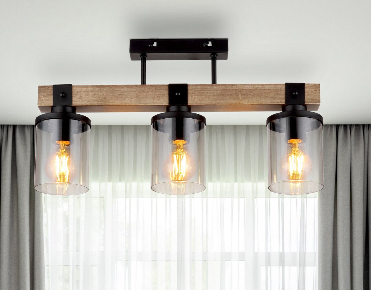 Moderne Deckenleuchte mit drei Glühbirnen in Glaszylindern, montiert auf einem Holzbalken, von unten betrachtet.