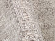 Nahaufnahme eines Designer Teppichs mit einem subtilen, gemusterten Design in Beige- und Grautönen, aus seitlicher Perspektive aufgenommen.