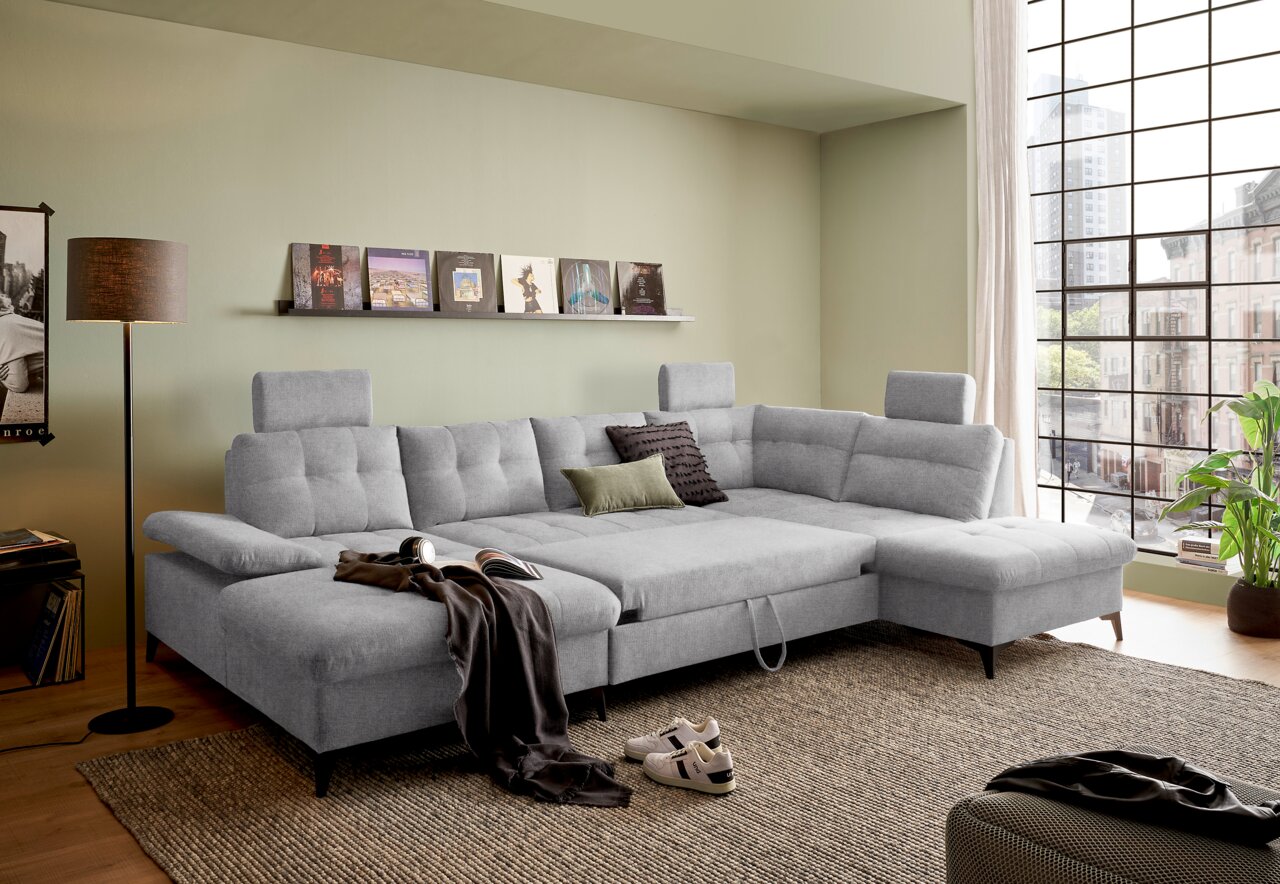 Graues Ecksofa in U-Form mit verstellbaren Kopfstützen, dekoriert mit Kissen, in einem modernen Wohnzimmer mit großen Fenstern. Perspektive von vorne.