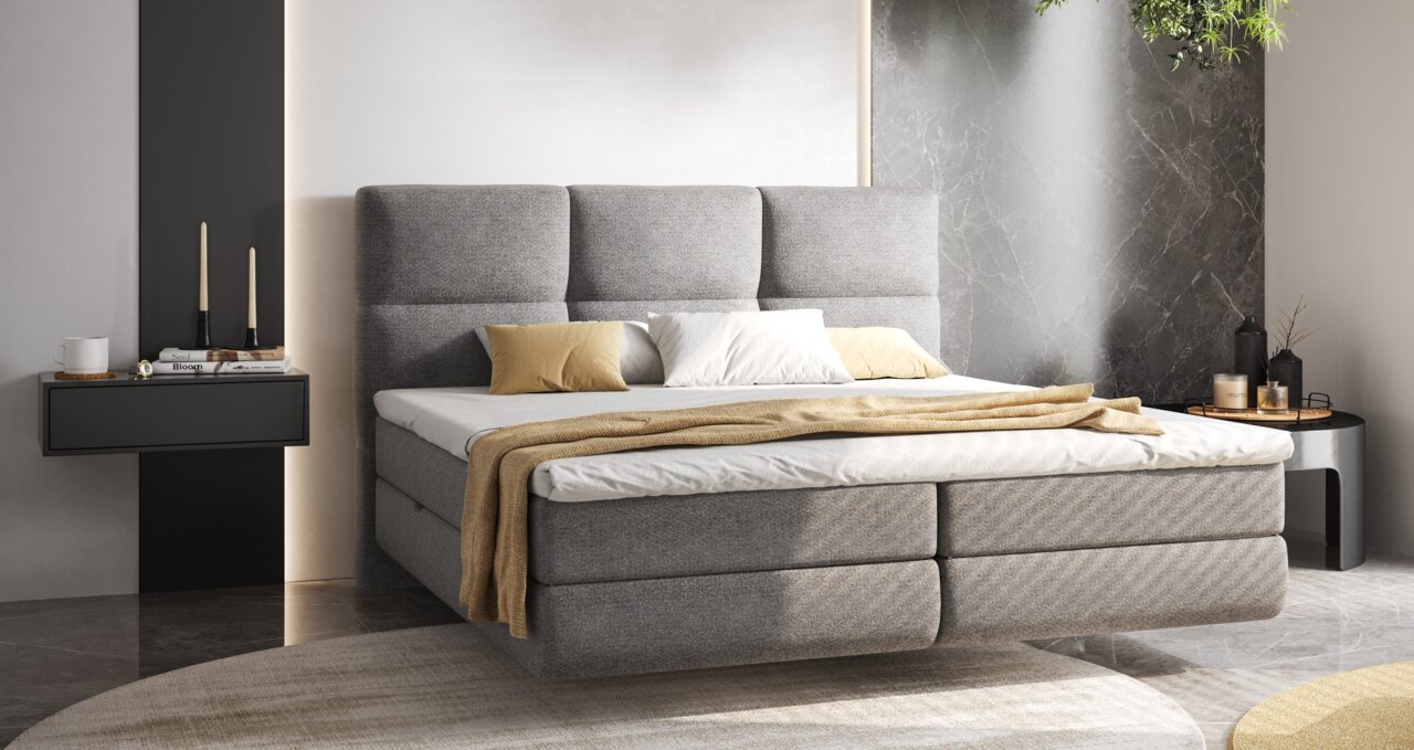 XORA Boxspringbed BENITO Modern boxspringbed met grijze bekleding en een hoog hoofdeinde, gezien vanaf de zijkant, gedecoreerd met kussens en een deken in neutrale tinten, in een stijlvolle slaapkamer.