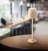 Moderne Akku-Tischleuchte Vannie auf einem Tisch in einem gemütlichen Café, seitliche Perspektive.