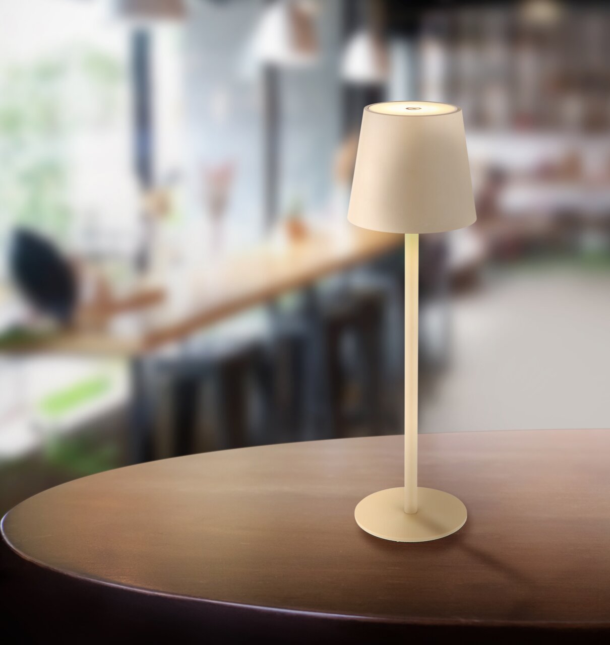 Moderne Akku-Tischleuchte Vannie auf einem Tisch in einem gemütlichen Café, seitliche Perspektive.