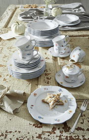 Ein stilvolles Kombiservice-Set mit floralem Muster, bestehend aus Tellern, Tassen und Untertassen, auf einem rustikalen Holztisch arrangiert. Die Perspektive zeigt das Set von oben, mit einem dekorativen Sternkeks auf einem Teller im Vordergrund.