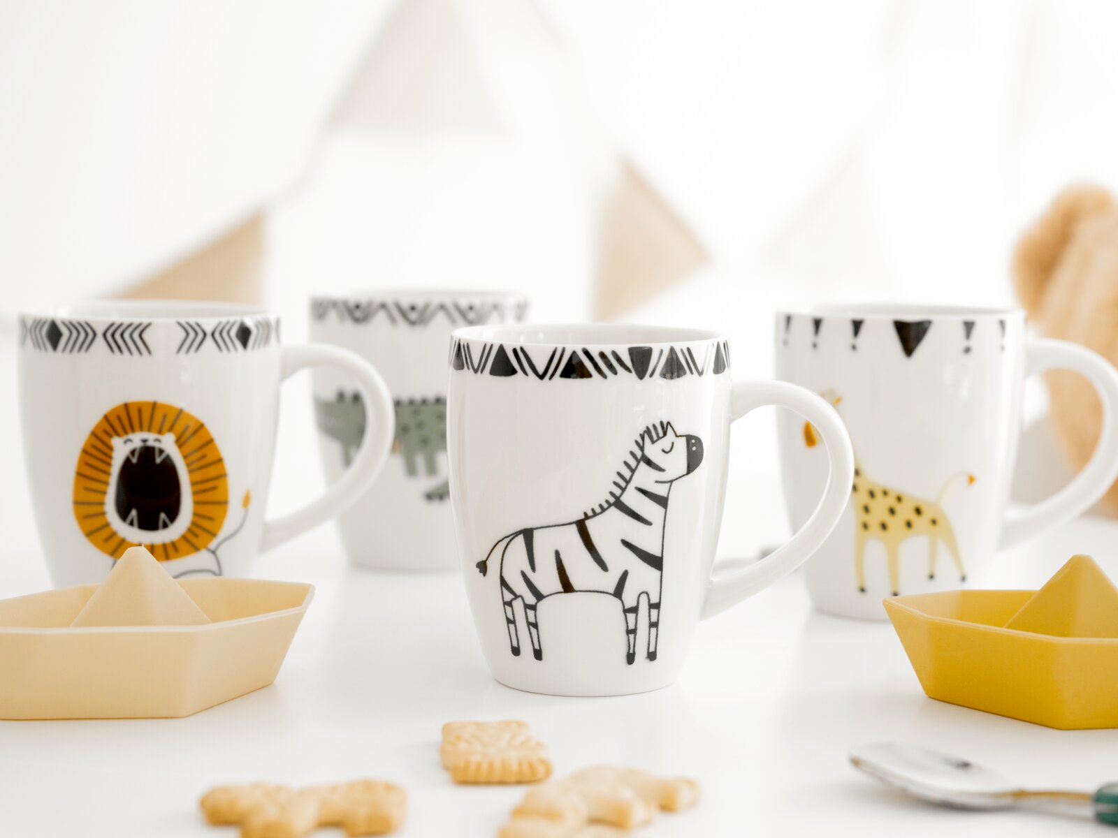 Weiße Keramiktasse mit handgezeichnetem Zebra und schwarzem Musterrand, frontal aus leichter Seitenperspektive zwischen weiteren Tiermotiv-Tassen arrangiert