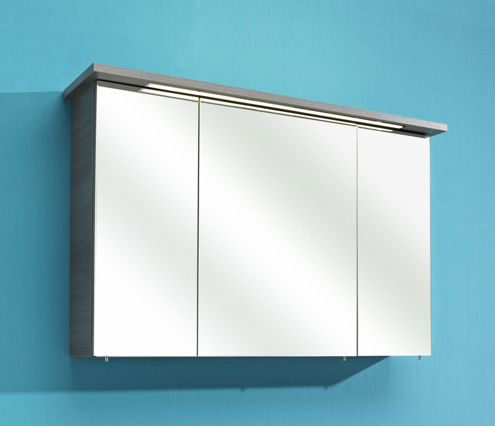 Moderner Spiegelschrank mit drei Türen, seitlicher Blickwinkel, montiert an einer blauen Wand.