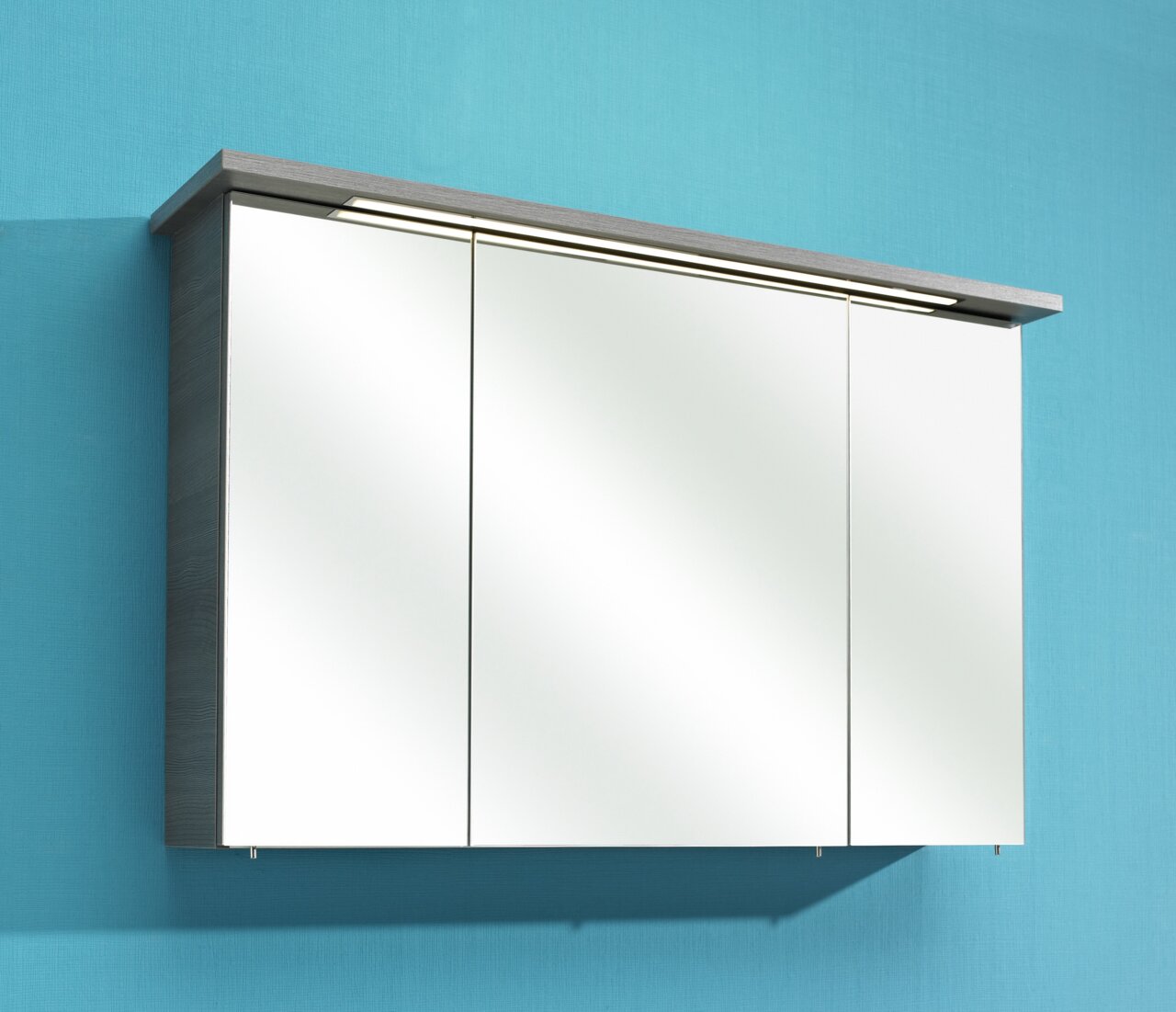 Moderne spiegelkast met drie deuren, zijaanzicht, bevestigd aan een blauwe muur.