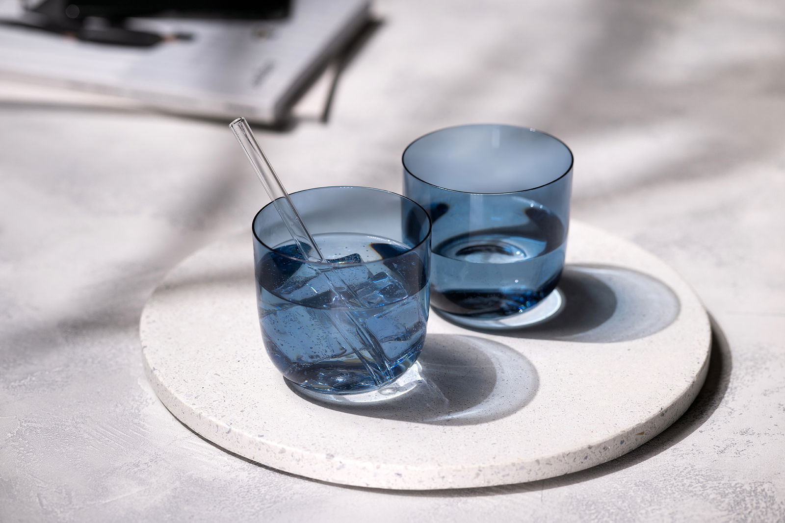 Like by Villeroy & Boch Wasserglas 2-tlg. LIKE ICE Zwei blaue Wassergläser auf einem runden, weißen Untersetzer, eines mit einem Glasstrohhalm und Eiswürfeln, aus der Vogelperspektive fotografiert.