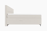 Seitenansicht eines modernen Boxspringbetts in hellem Beige mit hohem Kopfteil und schlanken schwarzen Füßen.
