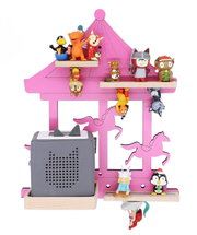 Vorderansicht eines pinken Karussell-Regals mit Pferde-Silhouetten und mehreren kleinen Tier- und Figuren-Miniaturen auf Holzablagen; links unten steht ein grauer Würfel-Lautsprecher in einer Holzschale.