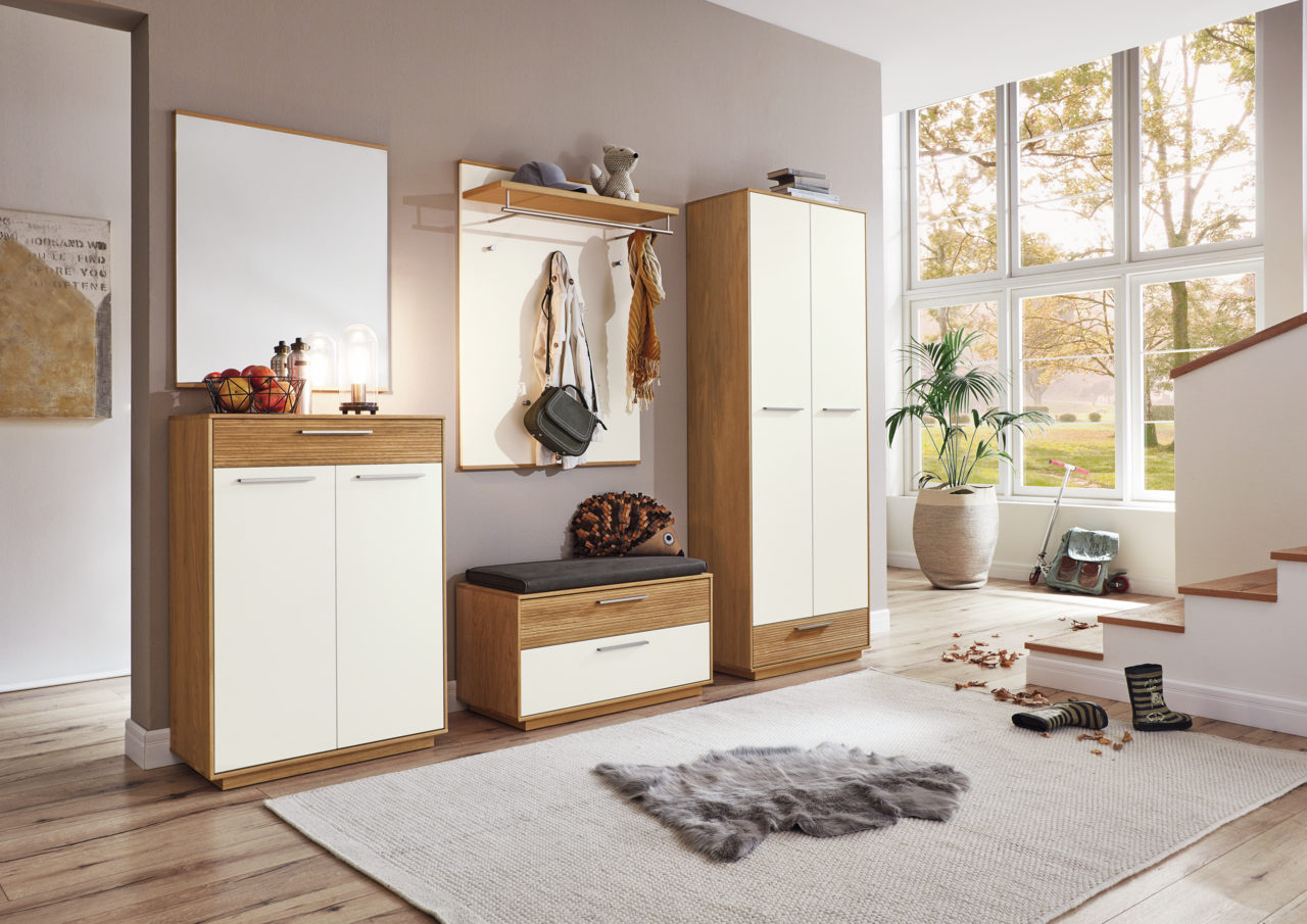 Moderne Garderobeneinrichtung mit Holz- und Weißakzenten, bestehend aus Schuhschrank, Sitzbank, Garderobenpaneel und Spiegel, in einem hellen Raum mit Blick auf große Fenster.