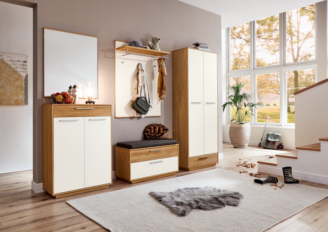 VOSS Halkast LOVENO Moderne garderobe-inrichting met houten en witte accenten, bestaande uit een schoenenkast, een bankje, een garderobepaneel en een spiegel, in een lichte ruimte met uitzicht op grote ramen.