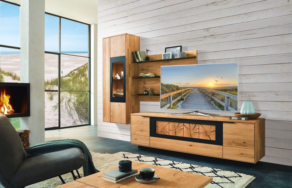 Moderne Wandkombination aus Holz in einem stilvollen Wohnzimmer mit Blick auf einen Strand durch große Fenster, seitliche Perspektive.