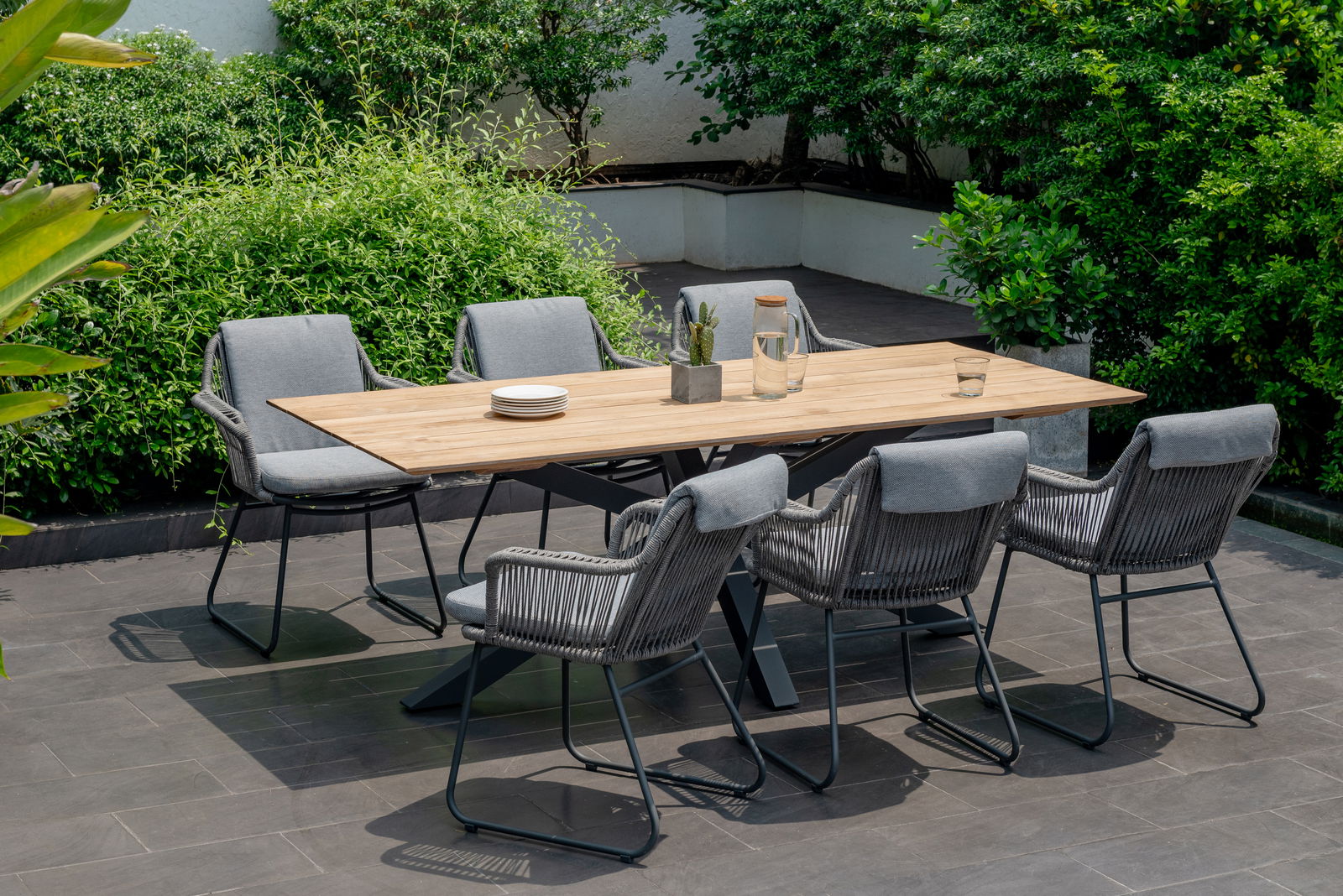Amatio Gartentisch GENET Moderner Gartentisch mit Holzplatte und sechs grauen Stühlen, umgeben von grüner Vegetation, aus der Vogelperspektive.