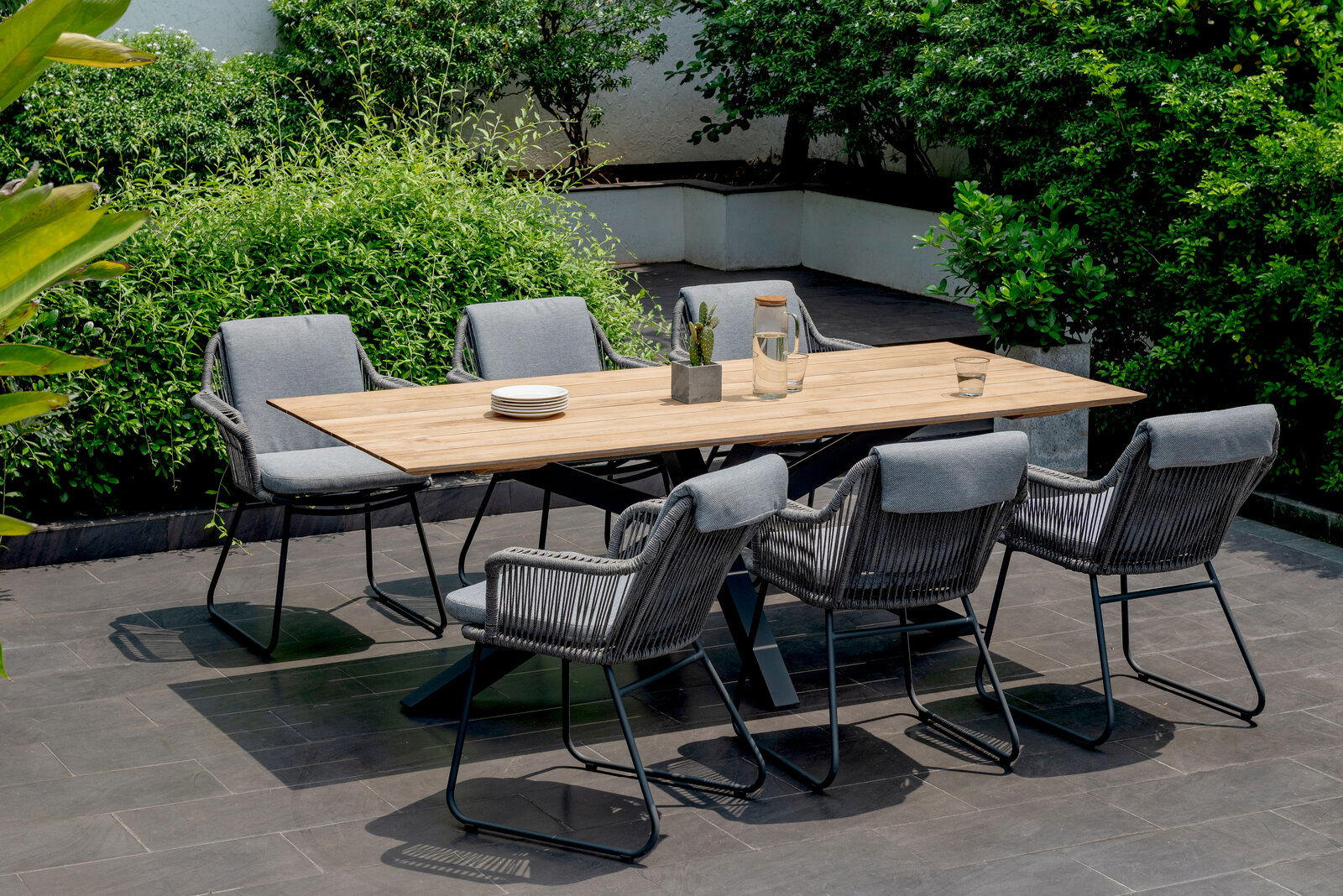 Moderner Gartentisch mit Holzplatte und sechs grauen Stühlen, umgeben von grüner Vegetation, aus der Vogelperspektive.