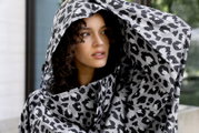 Nahaufnahme in 3/4-Ansicht: Model trägt eine schwarz-weiß gemusterte, voluminöse Kapuzenjacke mit Leopardenprint und blickt seitlich nach rechts.