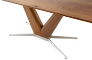 Close-up van een eettafel met een houten tafelblad en een moderne, V-vormige tafelpoot van hout en metaal, gezien vanaf de zijkant.