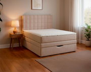 Beiges Boxspringbett mit gepolstertem, quadratisch gestepptem Kopfteil und weißer Matratzenauflage im modernen Schlafzimmer, seitliche Perspektive schräg von vorn