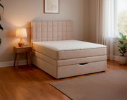 Beiges Boxspringbett mit gepolstertem, quadratisch gestepptem Kopfteil und weißer Matratzenauflage im modernen Schlafzimmer, seitliche Perspektive schräg von vorn