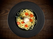 Spaghetti auf schwarzem Teller mit Kirschtomaten, geriebenem Käse und Kräutern auf Holztisch, Draufsicht