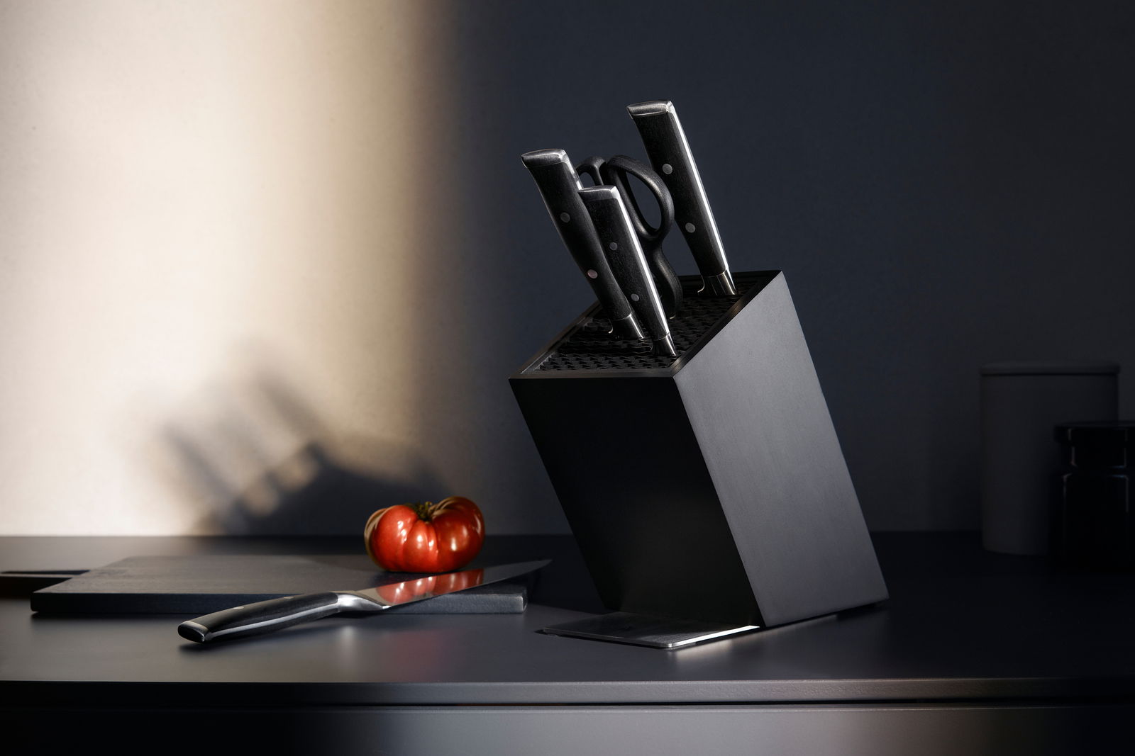 WMF Messerblock 6-tlg. GRAND CLASS Schrägansicht eines Messerblocks der Serie Grand Class mit mehreren Messern und einer Schere, auf einer Küchenarbeitsplatte neben einem Schneidebrett und einer Tomate.
