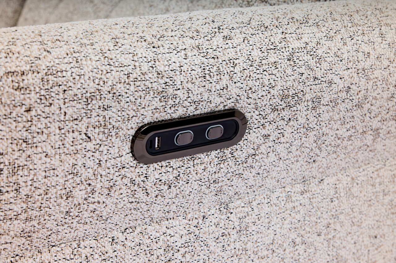 Nahaufnahme eines hellgrauen Stoffsofas mit integrierter USB-Ladebuchse und zwei Tasten, seitliche Perspektive.