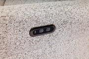 Nahaufnahme eines hellgrauen Stoffsofas mit integrierter USB-Ladebuchse und zwei Tasten, seitliche Perspektive.