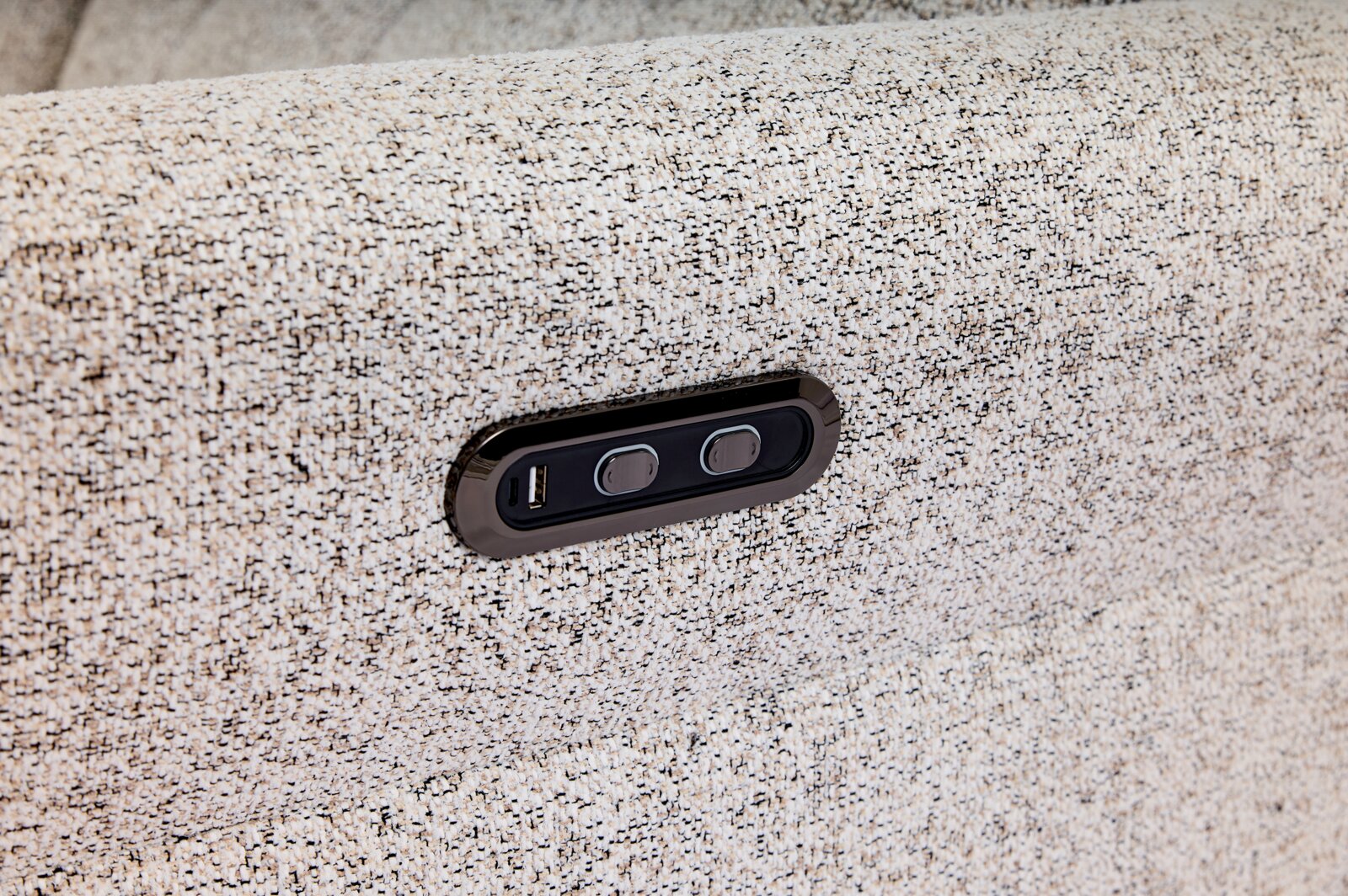Nahaufnahme eines hellgrauen Stoffsofas mit integrierter USB-Ladebuchse und zwei Tasten, seitliche Perspektive.