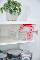 Rechteckige Glasbehälter mit roten Deckeln, gestapelt in einem weißen Küchenschrank, seitliche Perspektive