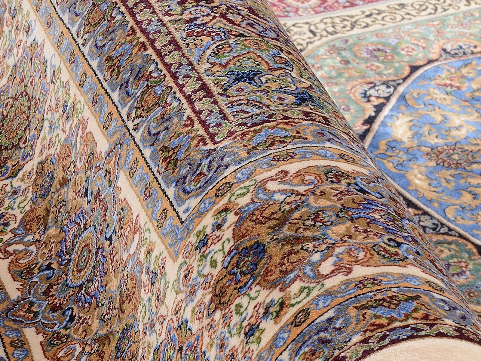 Nahaufnahme eines luxuriösen Orientteppichs mit detaillierten Mustern in Blau, Grün und Beige, perspektivisch von der Seite aufgenommen.