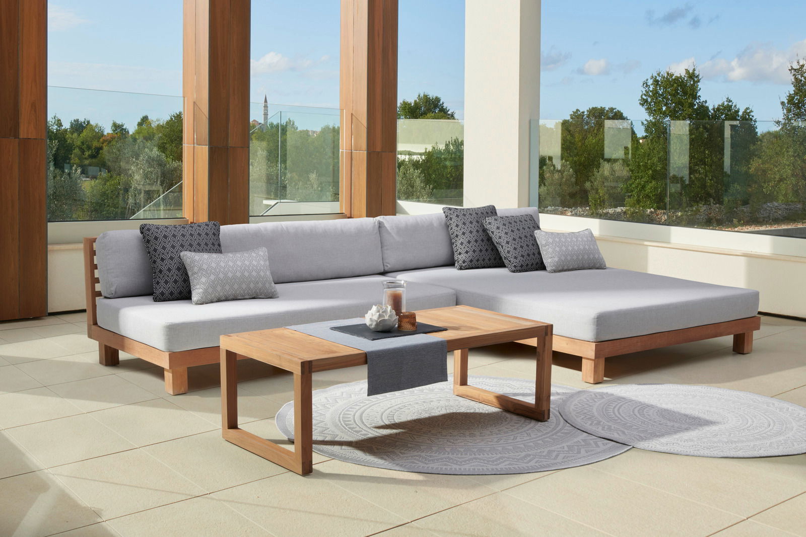 Modernes Loungesofa und Loungetisch aus Holz auf einer Terrasse mit Blick auf die Natur, seitliche Perspektive.
