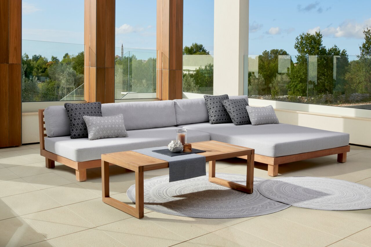 Moderne loungebank en houten salontafel op een terras met uitzicht op de natuur, zijaanzicht.