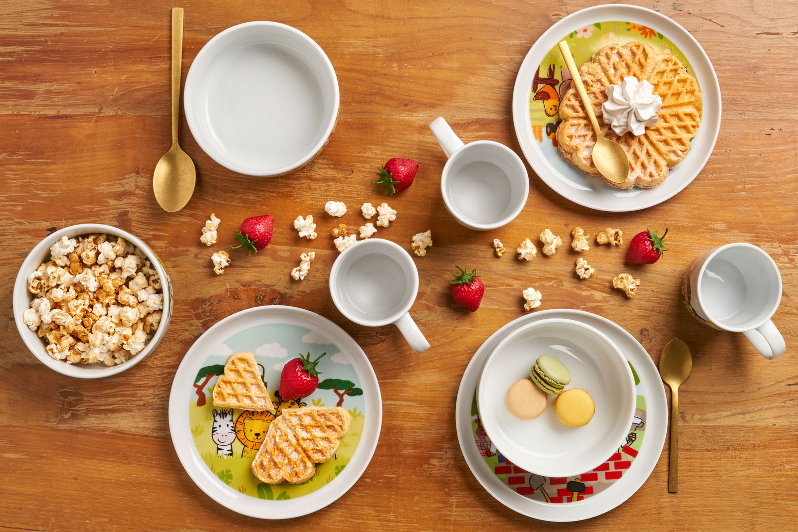 Vogelperspektive auf ein Kinder-Set mit Baustellenmotiv, bestehend aus Tellern, Schüsseln und Tassen, dekoriert mit Waffeln, Popcorn und Erdbeeren.
