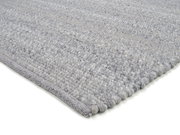 Nahaufnahme eines handgewebten Teppichs in Grautönen, von der Seite fotografiert, um die Textur und Webart zu zeigen.