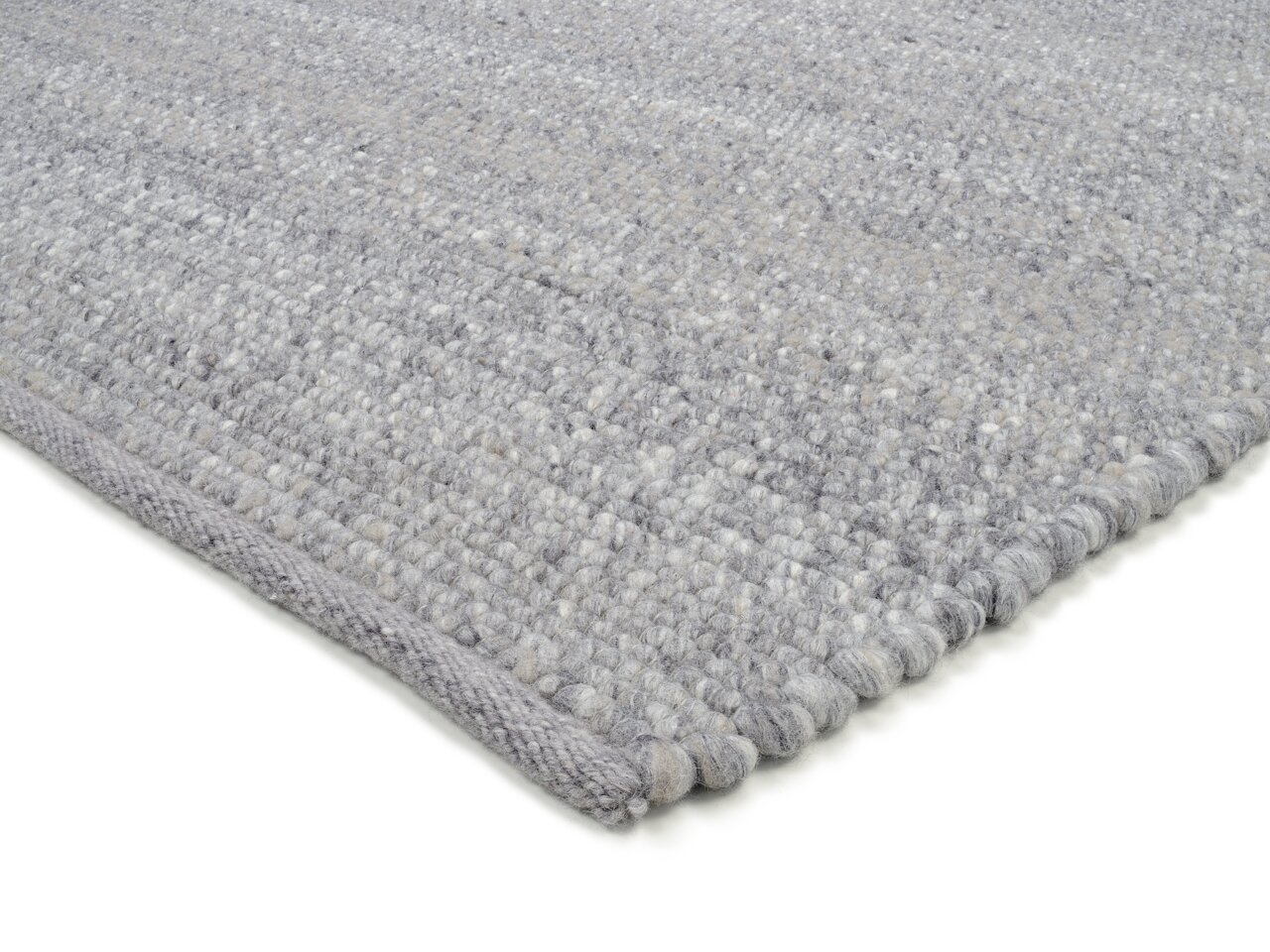 Nahaufnahme eines handgewebten Teppichs in Grautönen, von der Seite fotografiert, um die Textur und Webart zu zeigen.