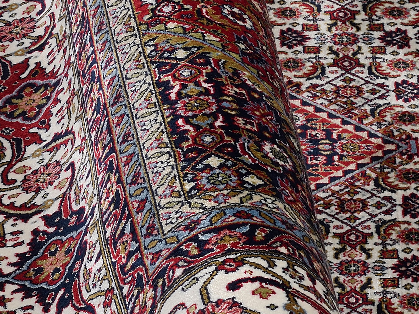 Detailansicht eines Orientteppichs mit komplexen Mustern in Rot, Blau und Cremefarben, teilweise aufgerollt.