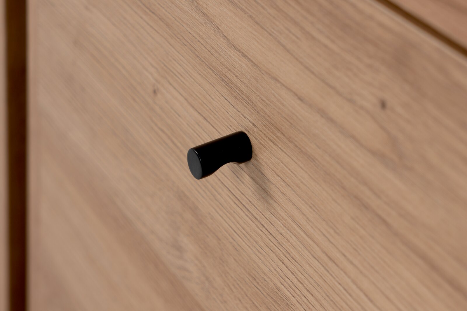 Nahaufnahme eines schwarzen Griffs auf einer Holzschublade, seitliche Perspektive