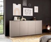 Modernes, niedriges Sideboard in Hellgrau mit vier Fronttüren vor dunkler Wand mit gerahmten Kunstdrucken; dekoriert mit Büchern, Vase und Teeset, aufgenommen in frontaler Perspektive leicht von links.