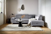 Graue Rundecke (L) in einem modernen Wohnzimmer, von vorne betrachtet, mit einem Beistelltisch, einer Lampe und einem Teppich.