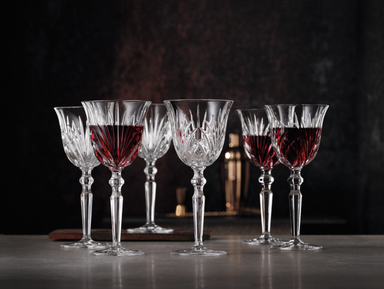 Nachtmann Rotweinkelch PALAIS Sechs elegante Rotweinkelche aus Kristallglas, teilweise gefüllt mit Rotwein, auf einem Tisch vor dunklem Hintergrund, seitliche Perspektive.
