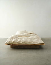 Minimalistisches Bett mit beiger Bettwäsche in Frontalansicht auf einem Holzboden.