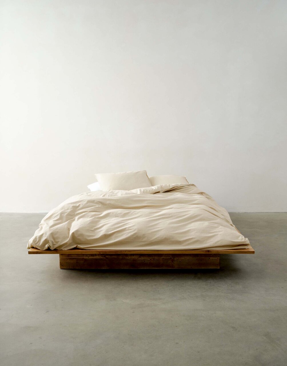 Minimalistisches Bett mit beiger Bettwäsche in Frontalansicht auf einem Holzboden.