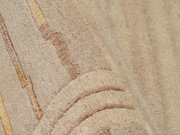 Nahaufnahme eines beigen Wollteppichs mit dezenten Streifenmustern in verschiedenen Brauntönen, perspektivisch von der Seite aufgenommen.