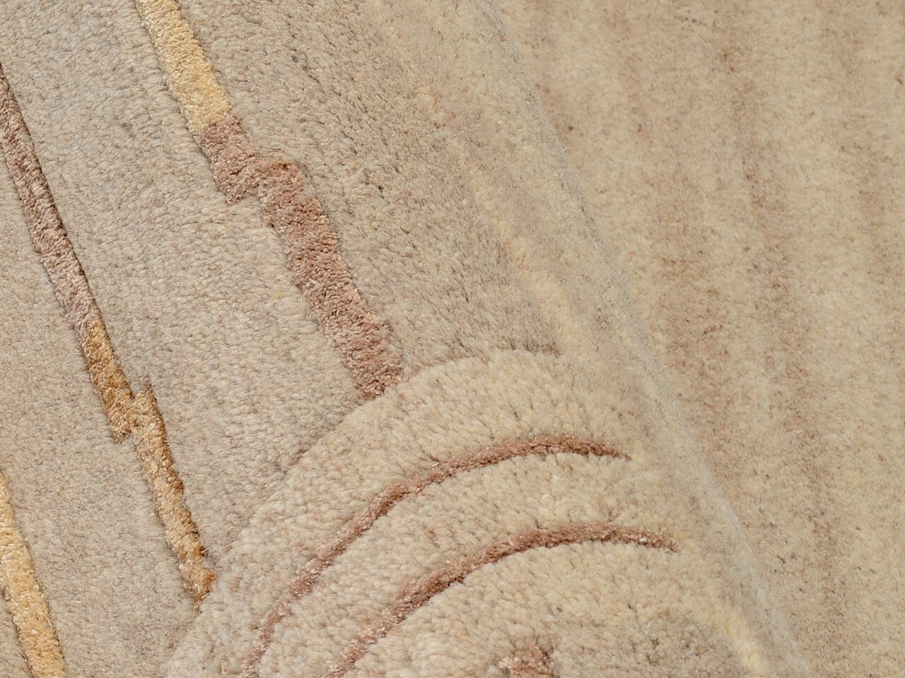 Nahaufnahme eines beigen Wollteppichs mit dezenten Streifenmustern in verschiedenen Brauntönen, perspektivisch von der Seite aufgenommen.
