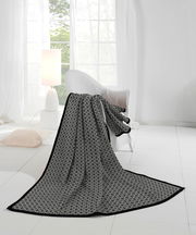 Elegante Wohndecke mit geometrischem Muster in einem hellen, modernen Raum, drapiert über einem Sessel, mit Blick auf ein großes Fenster.